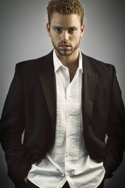 Açık beyaz gömlekli ve siyah ceketli bir adam kameraya bakıyor.