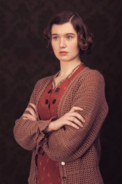 Kollarını kavuşturmuş, klasik kıyafetler giyen bir kadın.