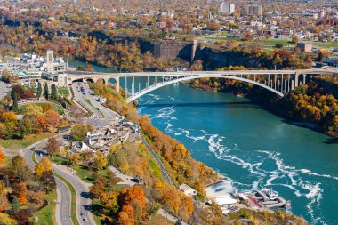 Niagara Şelalesi Şehri, Ontario, Kanada - 27 Ekim 2022: Sonbahar yeşillik mevsiminde güneşli bir günde Niagara Nehri Gökkuşağı Köprüsü.