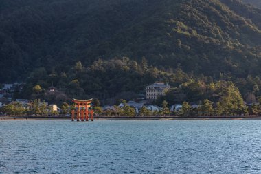 Feribottan Miyajima adasına bakıyorum. Yüzen kırmızı dev Grand O-Torii kapısı, güneşli bir günde dalgaların çekildiği körfez sahilinde duruyor, Hiroşima Şehri, Hiroşima Bölgesi, Japonya