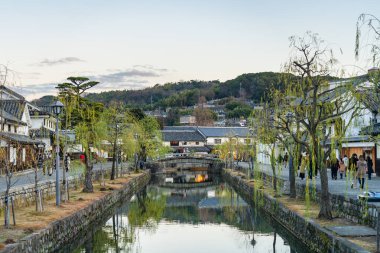 Okayama Bölgesi, Japonya - 27 Aralık 2019: Kurashiki Bikan Tarihi Bölgesi, alacakaranlıkta. Kentin tipik Japon yerleşim yerlerinin beyaz duvarları ve nehir kıyısında söğüt ağaçlarıyla bilinen manzarası.