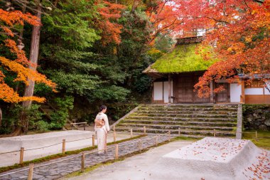 Kyoto, Japan. A woman wearing kimono in Honen-in Temple fall foliage garden. Maple trees turn red in autumn. Japanese traditional building and stone stairs in the background. Zen concept.