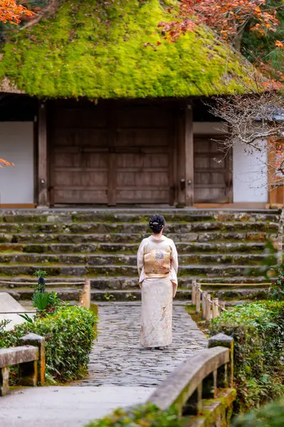 Kyoto, Japan. A woman wearing kimono in Honen-in Temple fall foliage garden. Maple trees turn red in autumn. Japanese traditional building and stone stairs in the background. Zen concept.