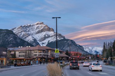 Banff, Alberta, Kanada - NOV 12020: sonbahar akşamı Banff Bulvarı sokak manzarası. Arka planda pembe gökyüzü olan Şelale Dağı karla kaplı..