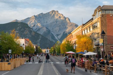 Banff, Alberta, Kanada - 28 Eylül 2020: Turistler sonbahar akşamı Banff Bulvarı 'nda yürüyüş ve yemek yiyorlar. Arka plandaki gül rengi gökyüzü üzerinde Cascade Dağı.