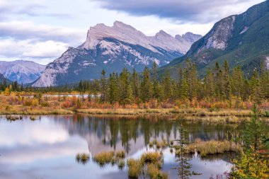 Alacakaranlıkta Vermilion Gölü sonbahar yeşillik manzarası. Banff Ulusal Parkı, Canadian Rockies, Alberta, Kanada. Kırmızı, sarı, altın renkli ağaçlar. Rundle Dağı, arka planda Sülfür Dağı..