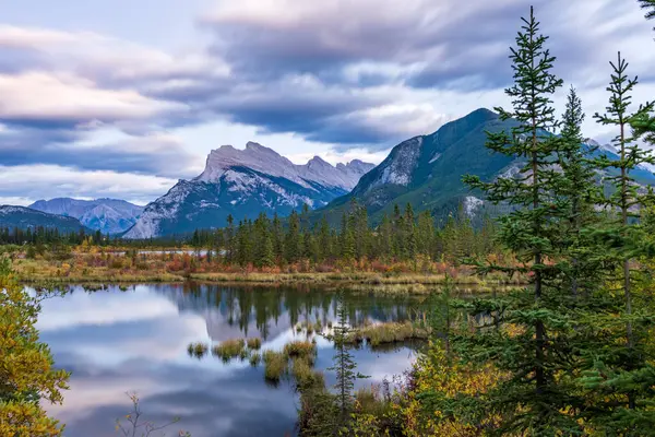 Alacakaranlıkta Vermilion Gölü sonbahar yeşillik manzarası. Banff Ulusal Parkı, Canadian Rockies, Alberta, Kanada. Turuncu, sarı, altın renkli ağaçlar. Rundle Dağı, arka planda Sülfür Dağı..