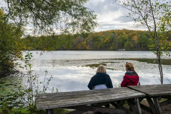 stock image People sitting on wooden benche by Moulin Lake (Lac du Moulin) enjoying the autumn scenery. Mont-Saint-Bruno National Park, Saint-Bruno-de-Montarville, Quebec, Canada.