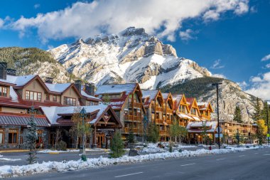 Banff, Kanada - 15: 2020 Banff Bulvarı karlı sonbahar güneşli bir günde. Arkasında beyaz bulutlar ve mavi gökyüzü olan karla kaplı Cascade Dağı. Banff Ulusal Parkı, Kanada Kayalıkları.