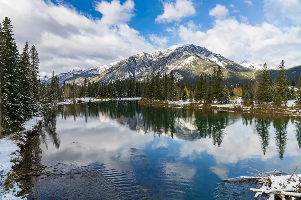 Banff Ulusal Parkı. Güneşli kış gününde güzel doğal manzara. Mavi gökyüzü ile Norquay Dağı, Bow River 'a ayna gibi yansıyan beyaz bulutlar. Banff Kasabası, Kanada Kayalıkları.