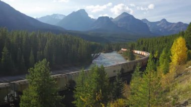 Alberta, Kanada - 4 Ekim 2022: Banff Ulusal Parkı Bow Nehri sonbahar manzarası. Morant Kavşağı 'ndaki yük treni. Kanada Kayalıkları güzel doğal manzara.