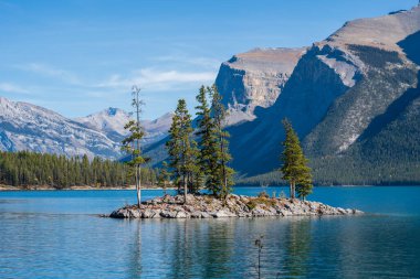 Banff Ulusal Parkı Minnewanka Gölü sonbahar manzarası. Köknar ağaçları olan bir kaya adası. Görkemli dağlar, mavi gökyüzüne karşı ormanlar. Alberta, Kanada. Kanada Kayalıkları güzel doğal manzara.