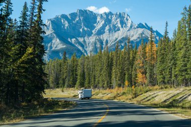 Sonbahar renk ormanlarında mavi gökyüzüne karşı manzaralı kır yolu. Minnewanka Gölü manzaralı sürüş, Banff Ulusal Parkı, Alberta, Kanada. Kanada Kayalıkları güzel doğal manzara.