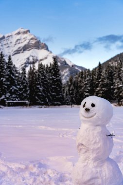 Karlı parkta gülümseyen bir kardan adam. Cascade Dağı ve arka planda ağaçlar. Banff Ulusal Parkı, Kanada Kayalıkları.