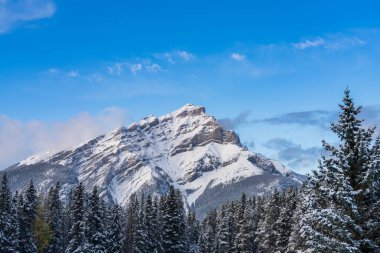 Karla kaplı Şelale Dağı 'nı mavi gökyüzü üzerinde karlı ormanla ve güneşli kış günlerinde beyaz bulutlarla kapatın. Banff Ulusal Parkı. Güzel manzara. Kanada Kayalıkları, Alberta, Kanada.