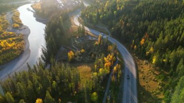 Sonbahar sabahı ormanın içindeki nehir boyunca yol manzarası. Bow River ve Three Sisters Parkway (742). Canmore, Alberta, Kanada.