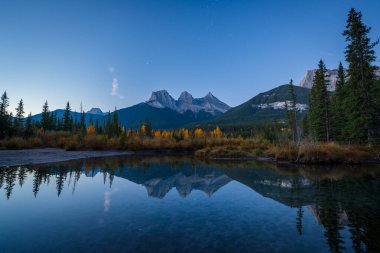 Sonbaharda şafak vakti Kanada Kayalıkları 'nın güzel manzarası. Dağ, sarı ve yeşil renkli orman suya yansıyor. Canmore, Alberta, Kanada. Üç Kız Kardeş Tepeler Üçlüsü.
