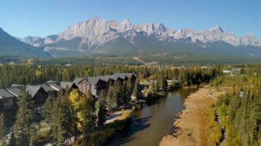 Sonbaharda arka planda dağlar olan çimlerin arasından geçen bir nehir. Spring Creek Boardwalk, Polis Deresi Yolu. Canmore, Alberta, Kanada.
