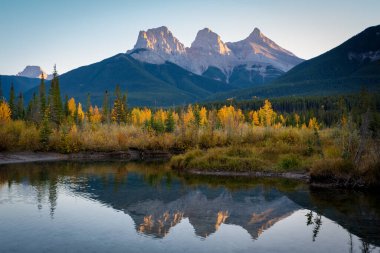 Sonbaharda şafak vakti Kanada Kayalıkları 'nın güzel manzarası. Dağ, sarı ve yeşil renkli orman suya yansıyor. Canmore, Alberta, Kanada. Üç Kız Kardeş Tepeler Üçlüsü.