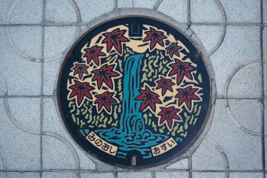 A colorful manhole cover design with waterfall and autumn maple leaves in Minoh city, Osaka, Japan. Translation: Minoh city water supply.  clipart