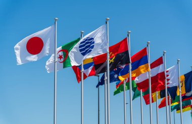 2025 Osaka Kansai Fuarı 'nın girişinde gökyüzünde uluslararası bayraklar dalgalanıyor.