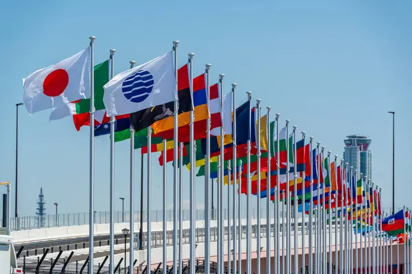 2025 Osaka Kansai Fuarı 'nın girişinde gökyüzünde uluslararası bayraklar dalgalanıyor.
