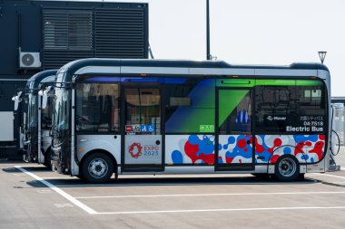 Osaka, Japonya - 30 Nisan 2025: 'E-nakliyeci' EV servis otobüsü hareket halinde, ziyaretçileri Dünya Fuarı 2025 sahasında naklediyor.