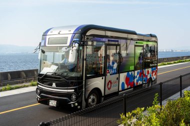 Osaka, Japonya - 30 Nisan 2025: 'E-nakliyeci' EV servis otobüsü hareket halinde, ziyaretçileri Dünya Fuarı 2025 sahasında naklediyor.