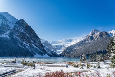 Fairmont Chateau Lake Louise 'de güneşli bir kış sabahı. Turkuaz renkli su yüzeyinde süzülen sis. Açık mavi gökyüzü, arka planda karla kaplı dağlar. Alberta, Kanada