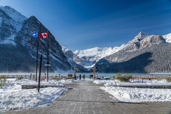Fairmont Chateau Lake Louise 'de güneşli bir kış sabahı. Turkuaz renkli su yüzeyinde süzülen sis. Açık mavi gökyüzü, arka planda karla kaplı dağlar. Alberta, Kanada