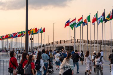 Osaka, Japonya - Haziran 12025: Dünya Fuarı 2025 Osaka, Kansai, Japonya 'dan ayrılan kalabalık Doğu Kapısı' nda dalgalanan uluslararası bayraklar altında alacakaranlıkta.