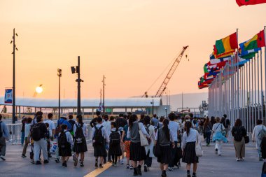 Osaka, Japonya - Haziran 12025: Dünya Fuarı 2025 Osaka, Kansai, Japonya 'dan ayrılan kalabalık Doğu Kapısı' nda dalgalanan uluslararası bayraklar altında alacakaranlıkta.