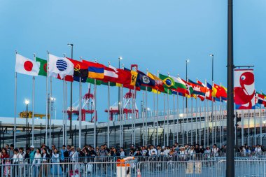 Osaka, Japonya - Haziran 12025: Dünya Fuarı 2025 Osaka, Kansai, Japonya 'dan ayrılan kalabalık Doğu Kapısı' nda dalgalanan uluslararası bayraklar altında alacakaranlıkta.