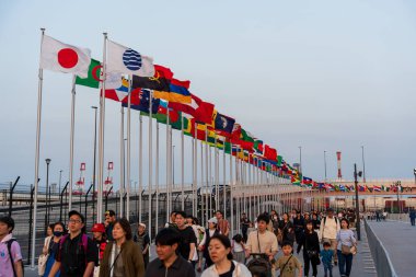 Osaka, Japonya - Haziran 12025: Dünya Fuarı 2025 Osaka, Kansai, Japonya 'dan ayrılan kalabalık Doğu Kapısı' nda dalgalanan uluslararası bayraklar altında alacakaranlıkta.