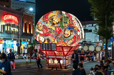 Hirosaki, Aomori, Japonya - 5 Ağustos 2024: Hirosaki Neputa Festivali. Uçsuz bucaksız ve aydınlık hayran şekilli Neputa şamandırası bir müzik grubuyla birlikte sokaklarda süzülüyor..