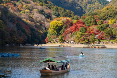 Turistler, sonbaharda Oi Nehri ve Arashiyama 'daki Katsura Nehri' nde, Kyoto, Japonya 'da Rankyo Boğazı manzaralı Yakatabune tekne turunun keyfini çıkarıyorlar..