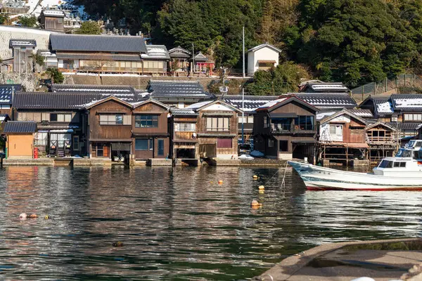 Ine, Kyoto, Japonya - 25 Şubat 2025: Ine Körfezi 'nde gezici bir tekne turistleri balıkçı köyünün rıhtımındaki tarihi Funaya kayıkhanelerinden geçirir..