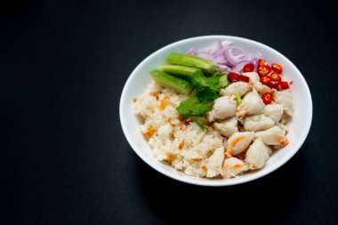 Üzeri sarımsaklı pirinç buğulanmış yengeç eti, arpacık soğanı, salatalık ve siyah arka planda kırmızı biber.