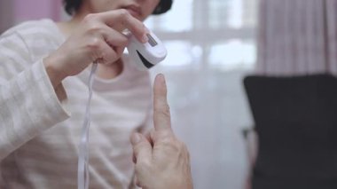 Yakın çekim, Ağır çekim. Kadın, evdeki nefes borusu ameliyatı geçiren hastaya oksijen ölçer ve hastanın kanındaki oksijen seviyesini ölçer..