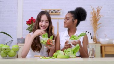 Siyah ve beyaz genç arkadaşlar mutfakta sebze salatası yapmak için birlikte çalışıyorlar. Sağlıklı yemek..