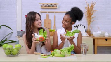 Siyah ve beyaz genç arkadaşlar mutfakta sebze salatası yapmak için birlikte çalışıyorlar. Sağlıklı yemek..