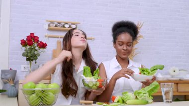 Siyah ve beyaz genç arkadaşlar mutfakta sebze salatası yapmak için birlikte çalışıyorlar. Sağlıklı yemek..