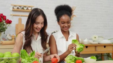 Siyah ve beyaz genç arkadaşlar mutfakta sebze salatası yapmak için birlikte çalışıyorlar. Sağlıklı yemek..