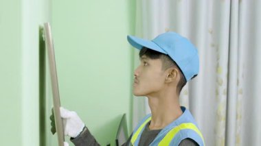 Asyalı genç teknisyen yeşil yatak odasına makyaj aynası yerleştiriyor.