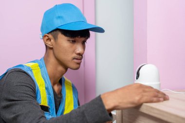 Asyalı erkek teknisyen, müşterinin evindeki akıllı telefonu kullanarak CCTV veya kablosuz güvenlik kameralarını kurar ve kurar.