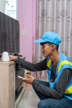 Asyalı erkek teknisyen, müşterinin evindeki akıllı telefonu kullanarak CCTV veya kablosuz güvenlik kameralarını kurar ve kurar.