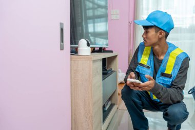 Asyalı erkek teknisyen, müşterinin evindeki akıllı telefonu kullanarak CCTV veya kablosuz güvenlik kameralarını kurar ve kurar.