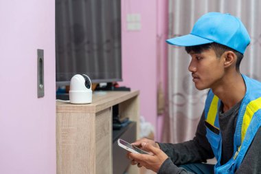 Asyalı erkek teknisyen, müşterinin evindeki akıllı telefonu kullanarak CCTV veya kablosuz güvenlik kameralarını kurar ve kurar.