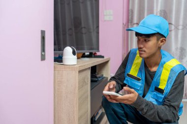 Asyalı erkek teknisyen, müşterinin evindeki akıllı telefonu kullanarak CCTV veya kablosuz güvenlik kameralarını kurar ve kurar.