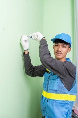 Asyalı erkek işçi alçı taşı duvarındaki vidaları sıkmak için tornavida kullanıyor.